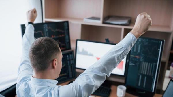 Hands up because of success. Man working o<em></em>nline in the office with multiple computer screens in index charts